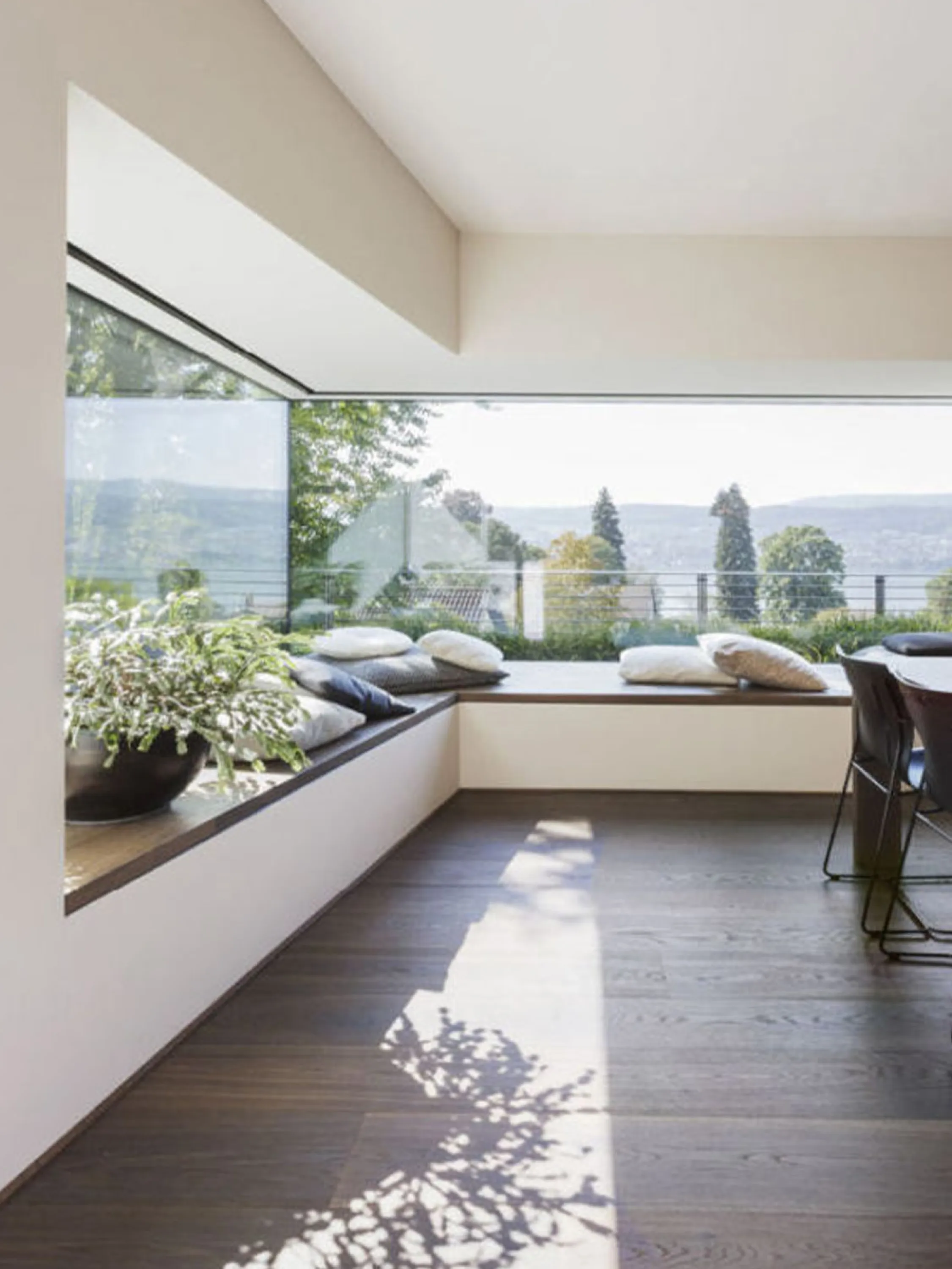 Angular bay window with shadows from the outdoor greenery projected on the floor.