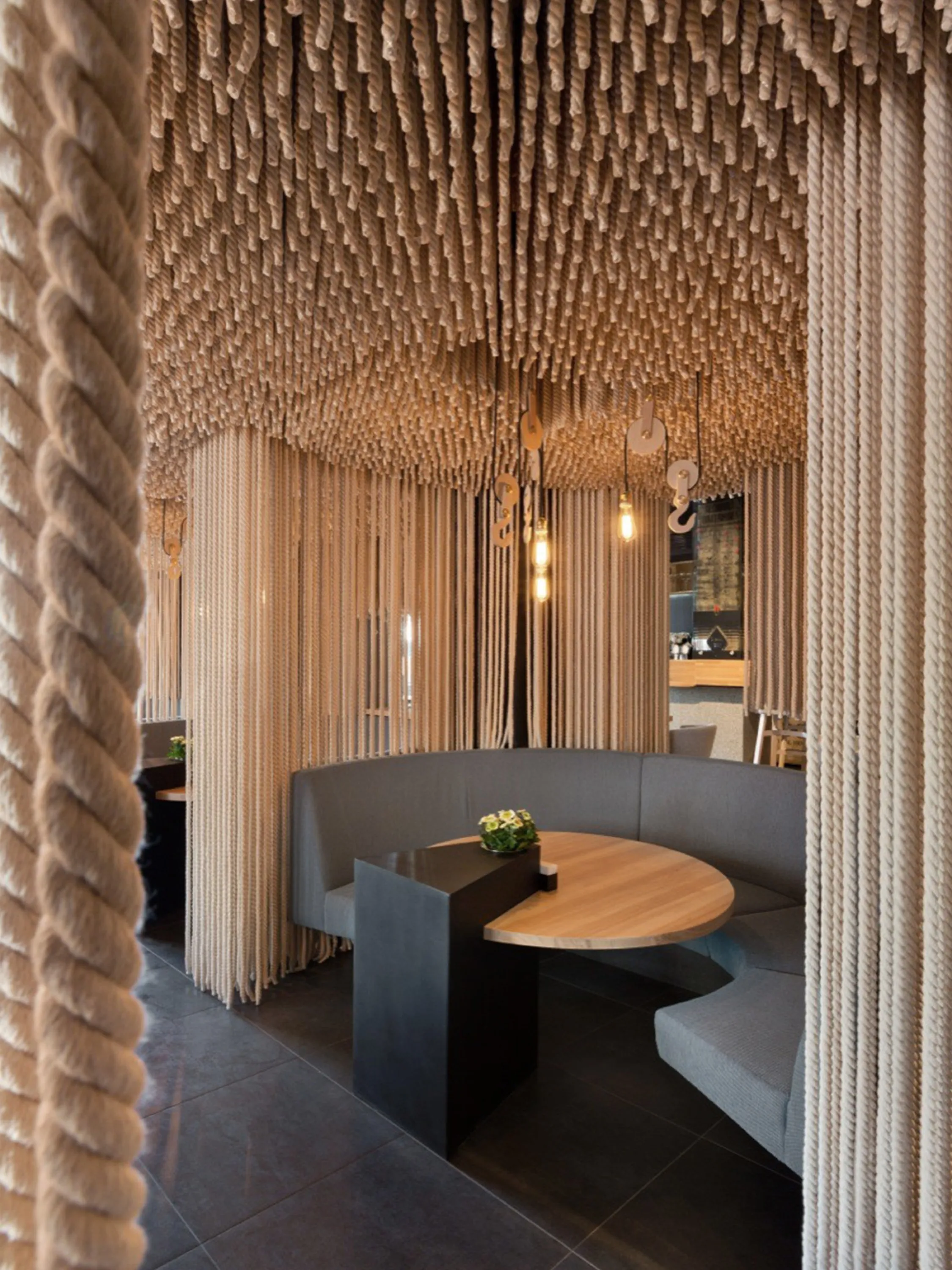 Restaurant tables separated by thick ropes hanging from the ceiling.