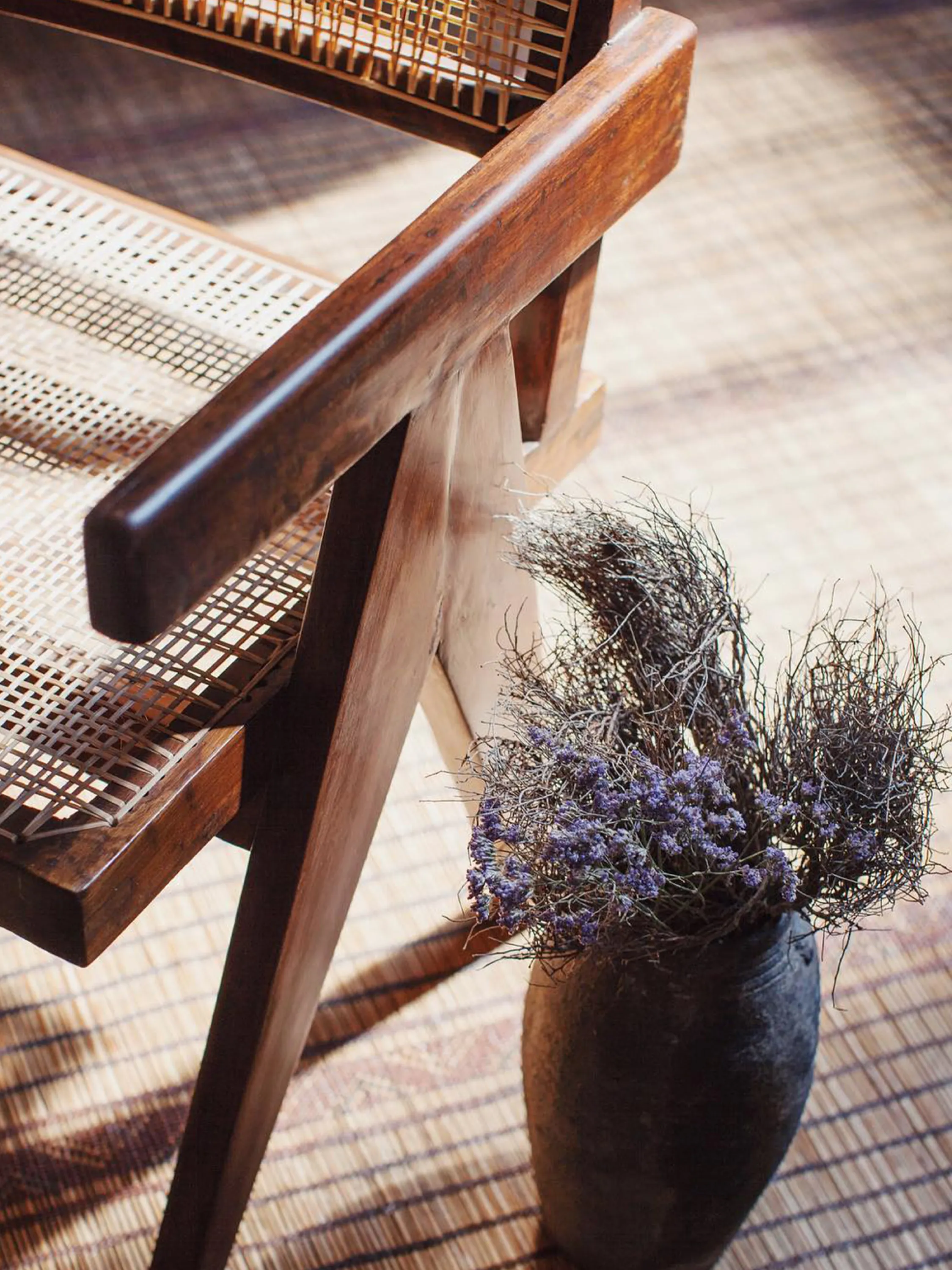 Close-up of a wood & rattan chair, a natural fibre rug, and flowers in a vase.