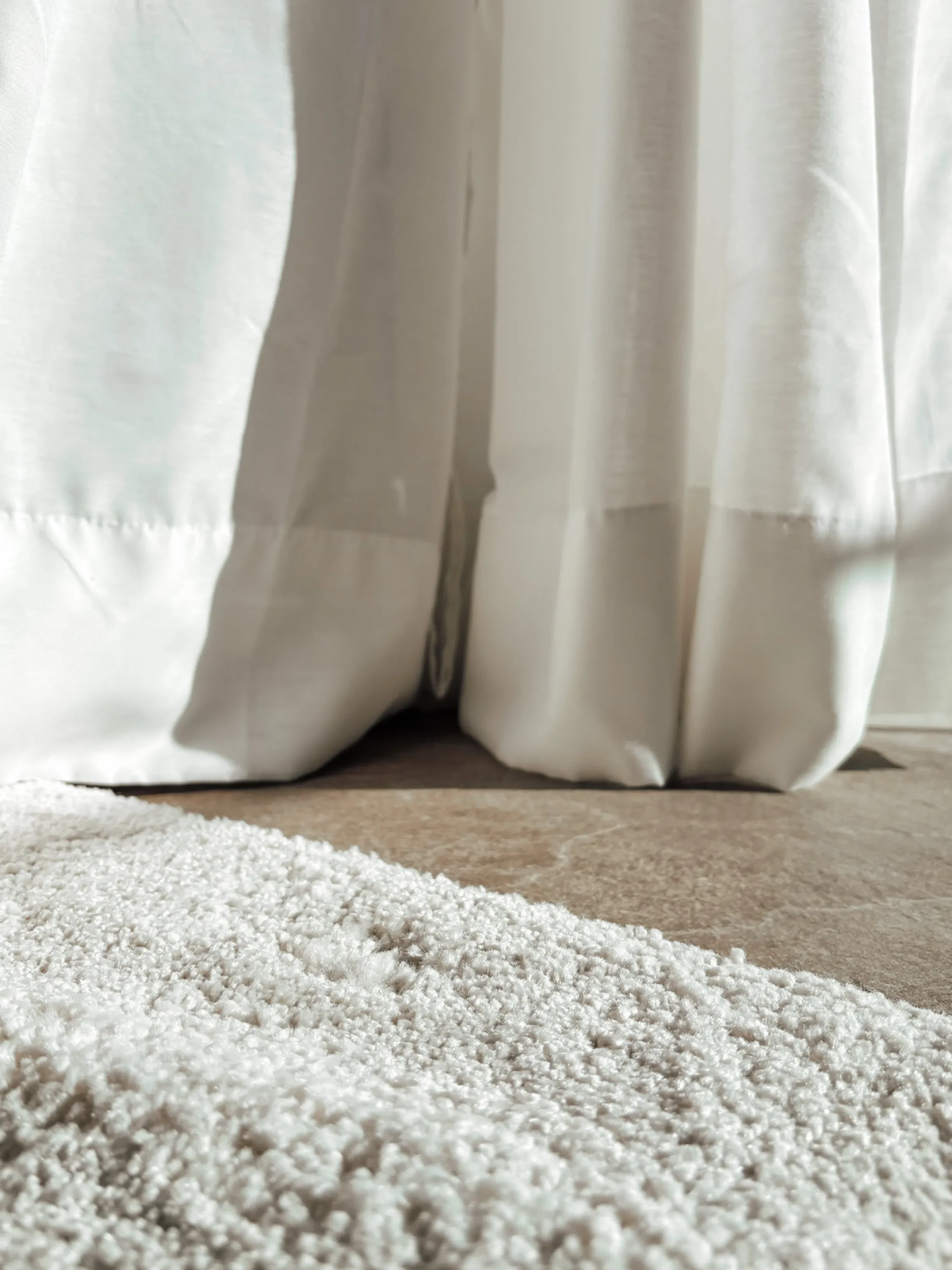 Lightweight curtains and textured rug hit by the sun.