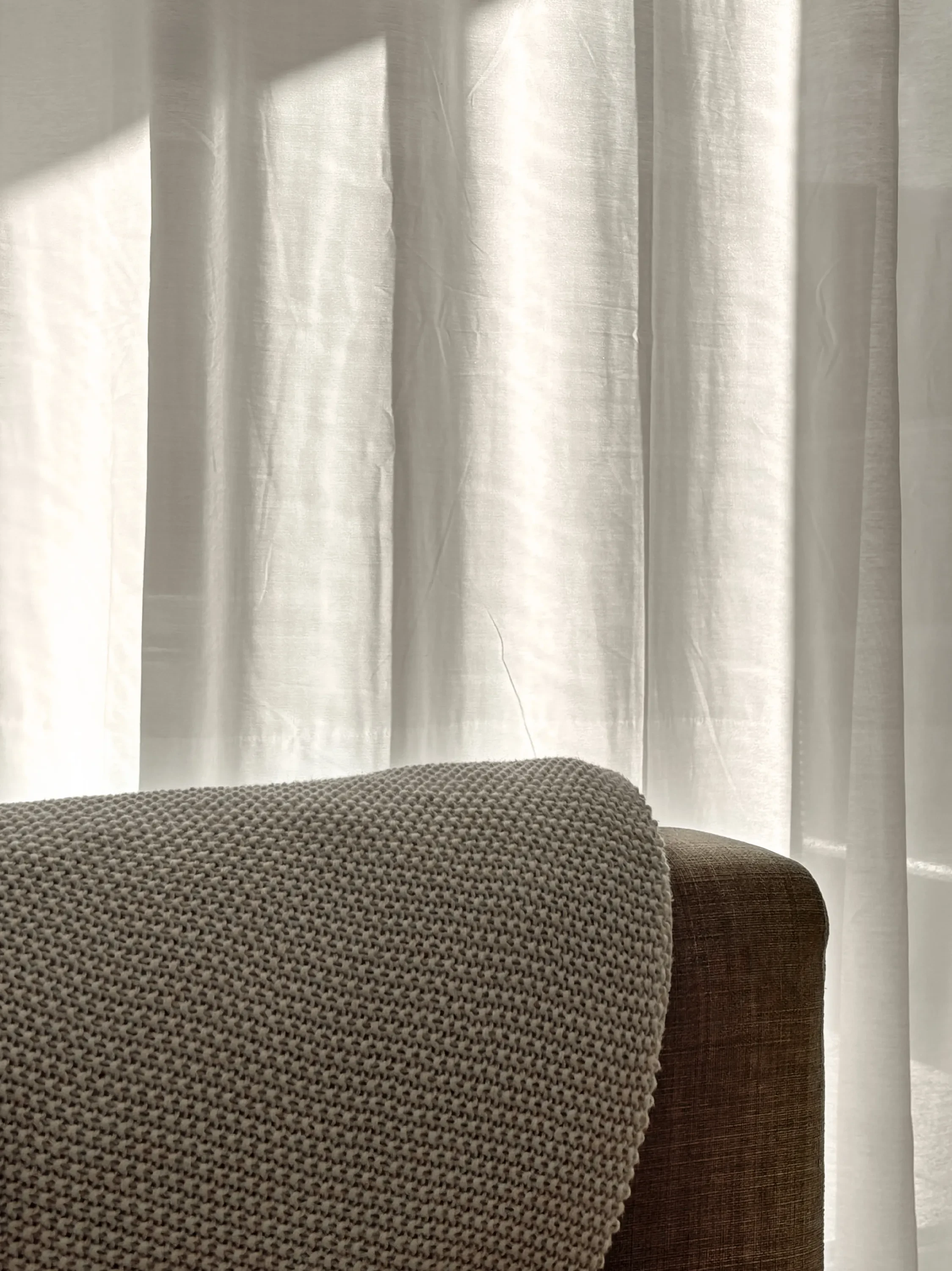 Sofa and clear curtains hit by the sun.