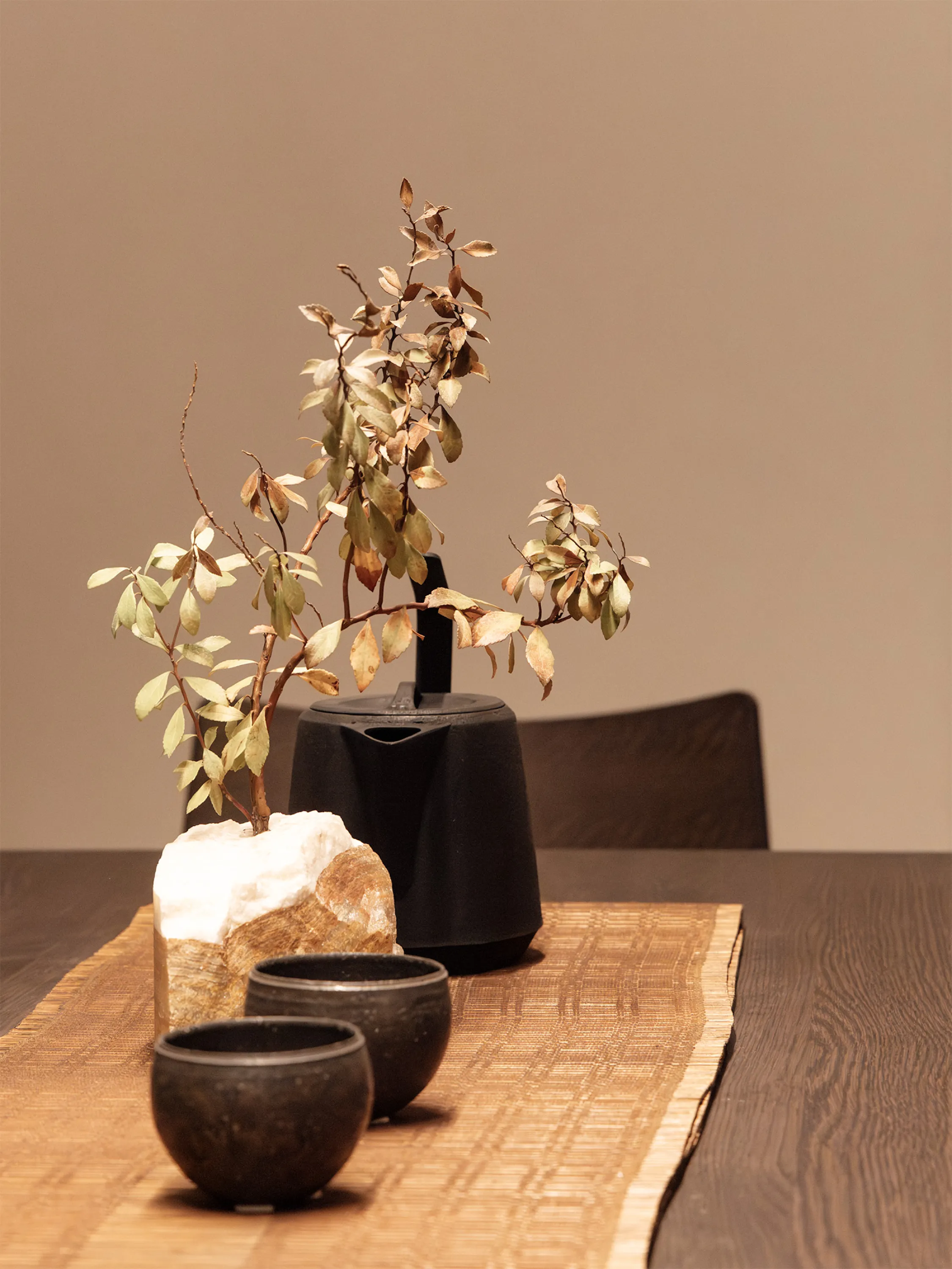 Textural table styling with stones, a branch, clay teapot and cups, and a bamboo mat.