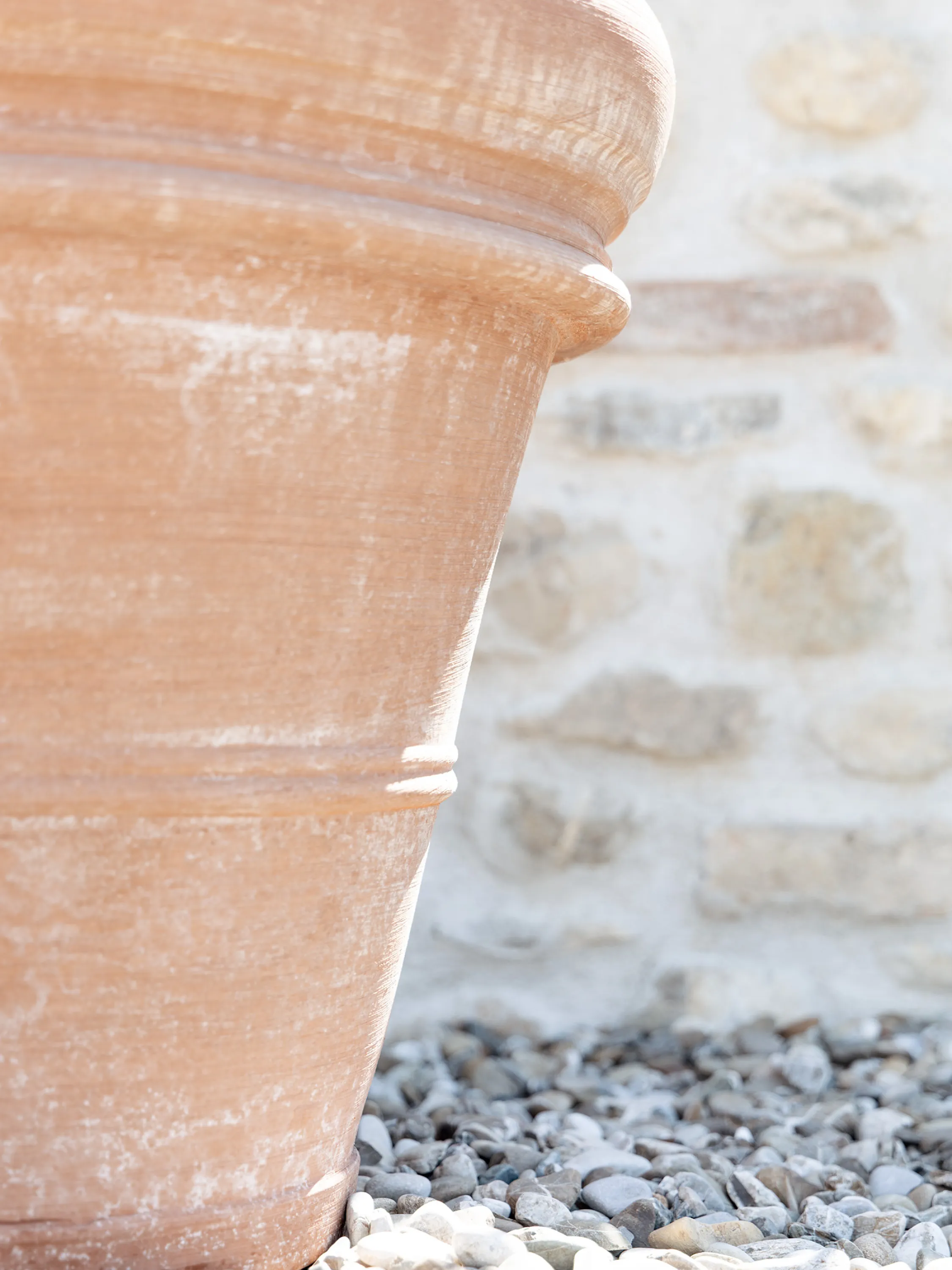 A large terracotta plant pot beside a stone wall, warmed by late-afternoon sun.
