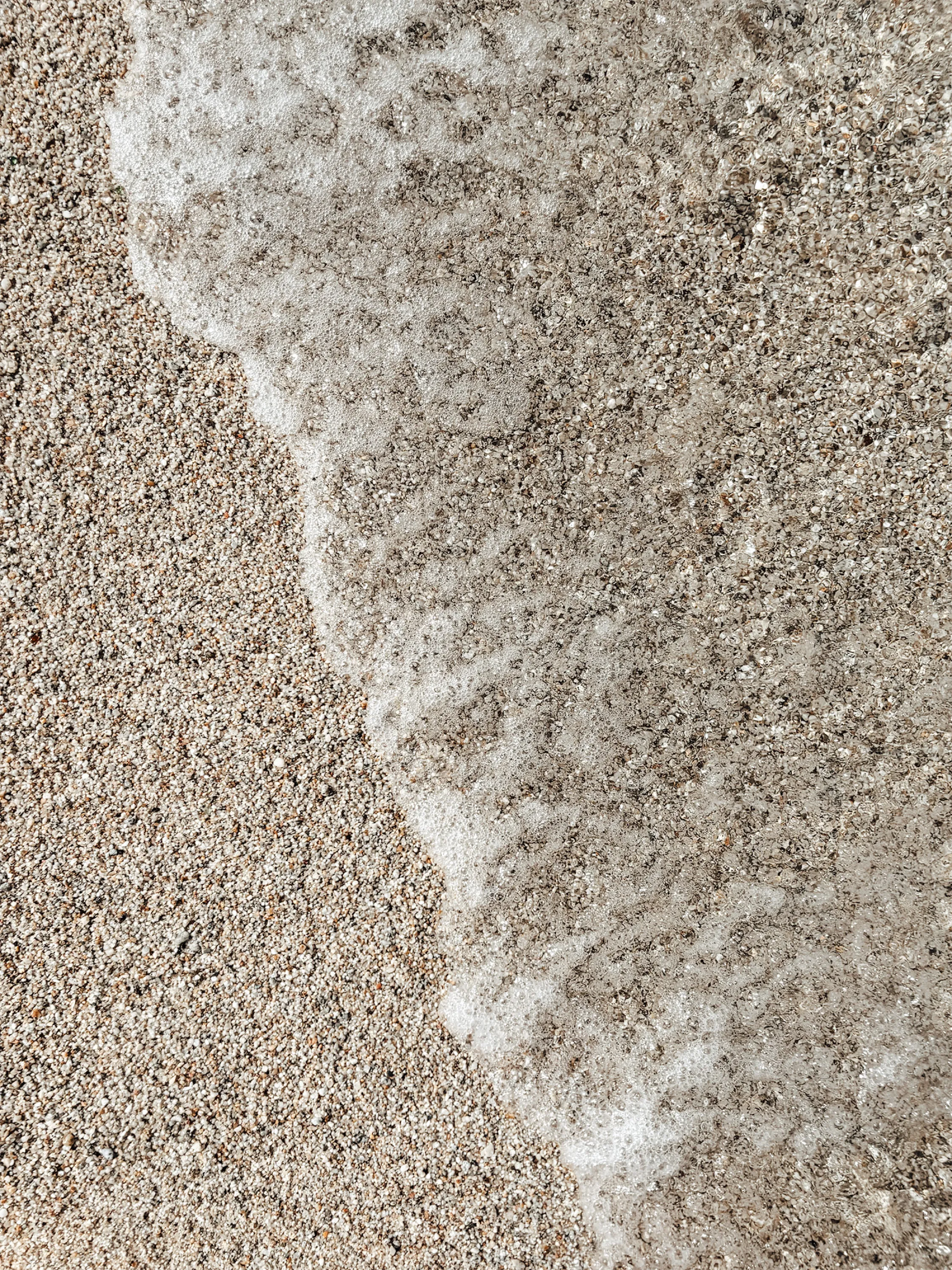 Overhead view of sea foam meeting dry sand along a curving edge.
