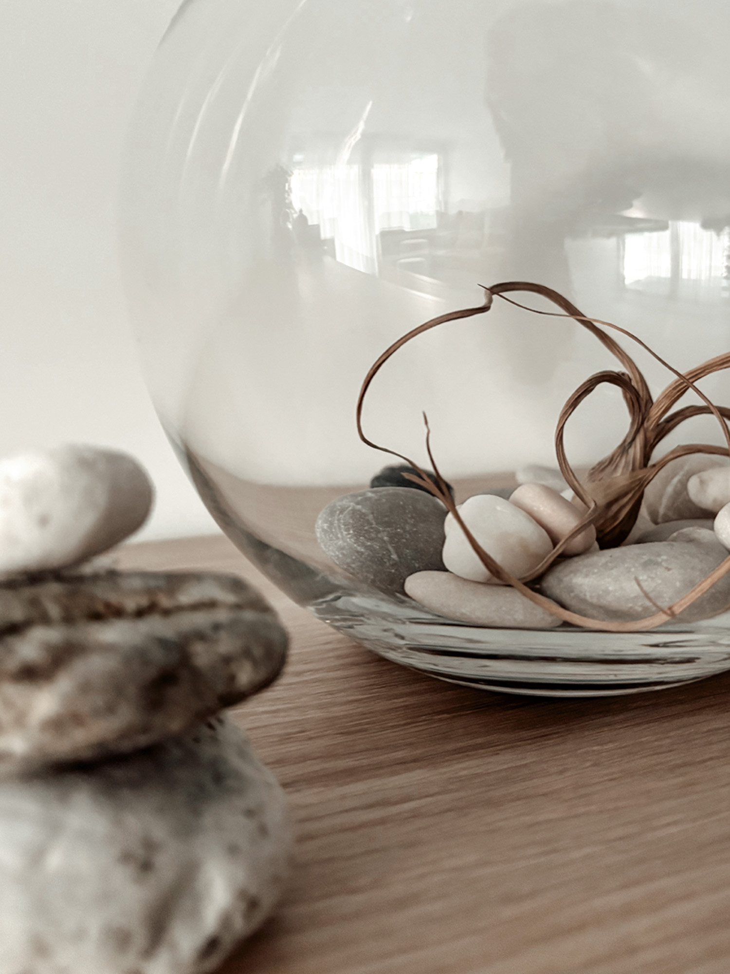 Pebbles and a dry grass strand gathered in a glass sphere on an oak surface