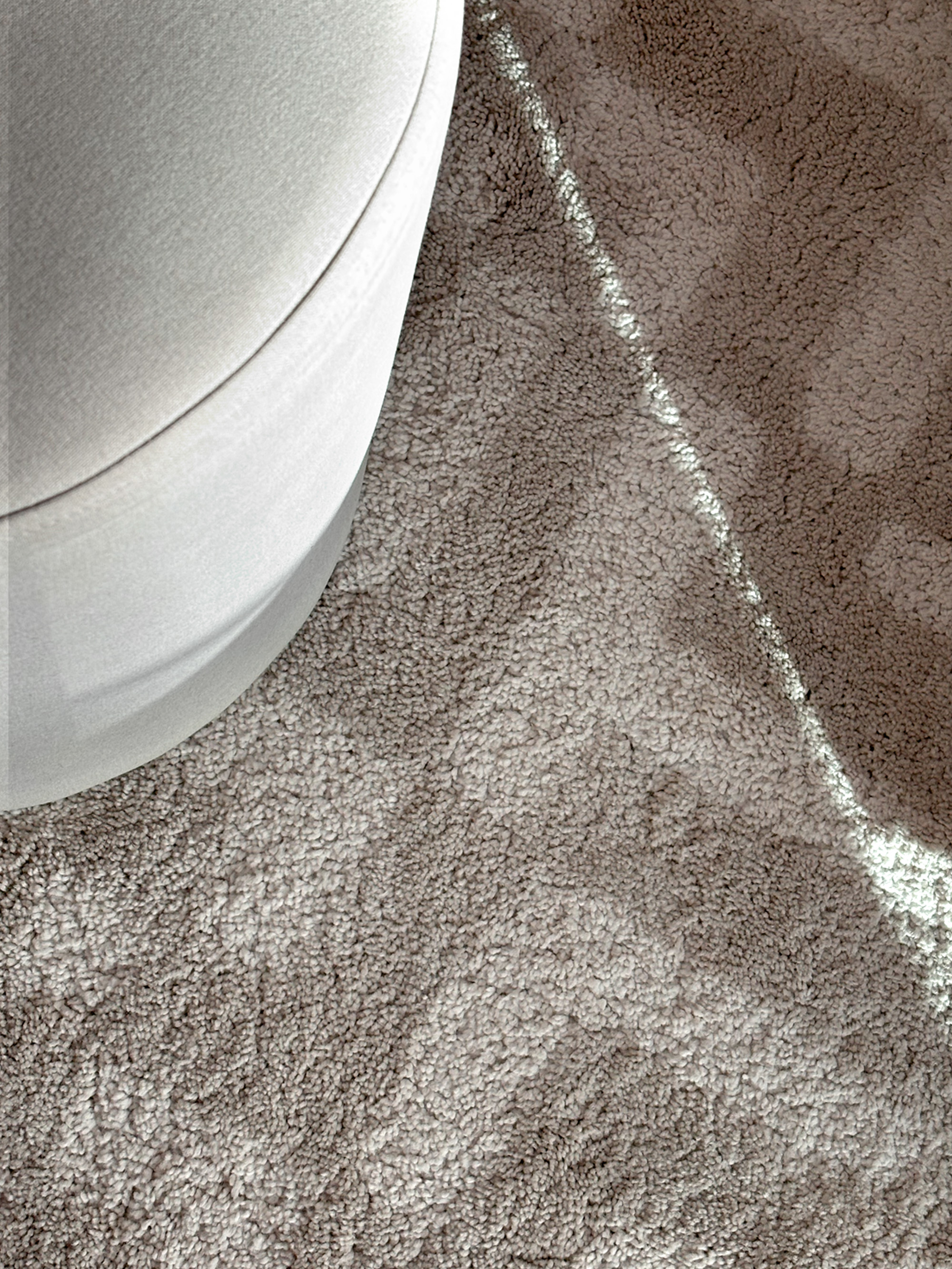 Sunlight tracing the edge of a sand-toned rug beside a cream upholstered pouf
