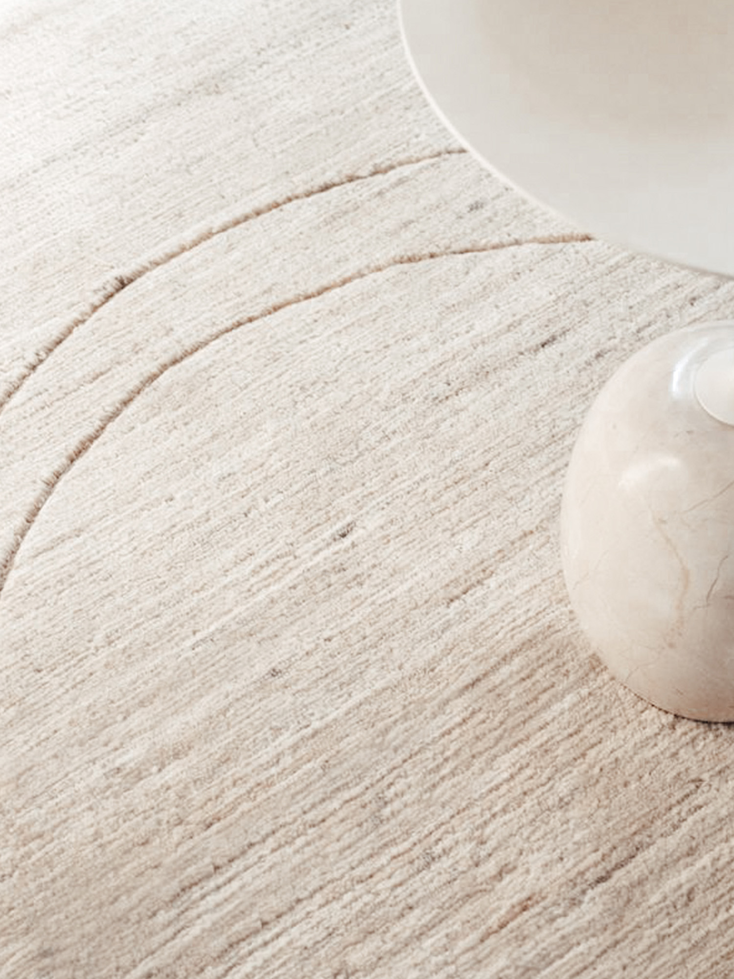 Hand-knotted cream rug with a carved arc and a marble object