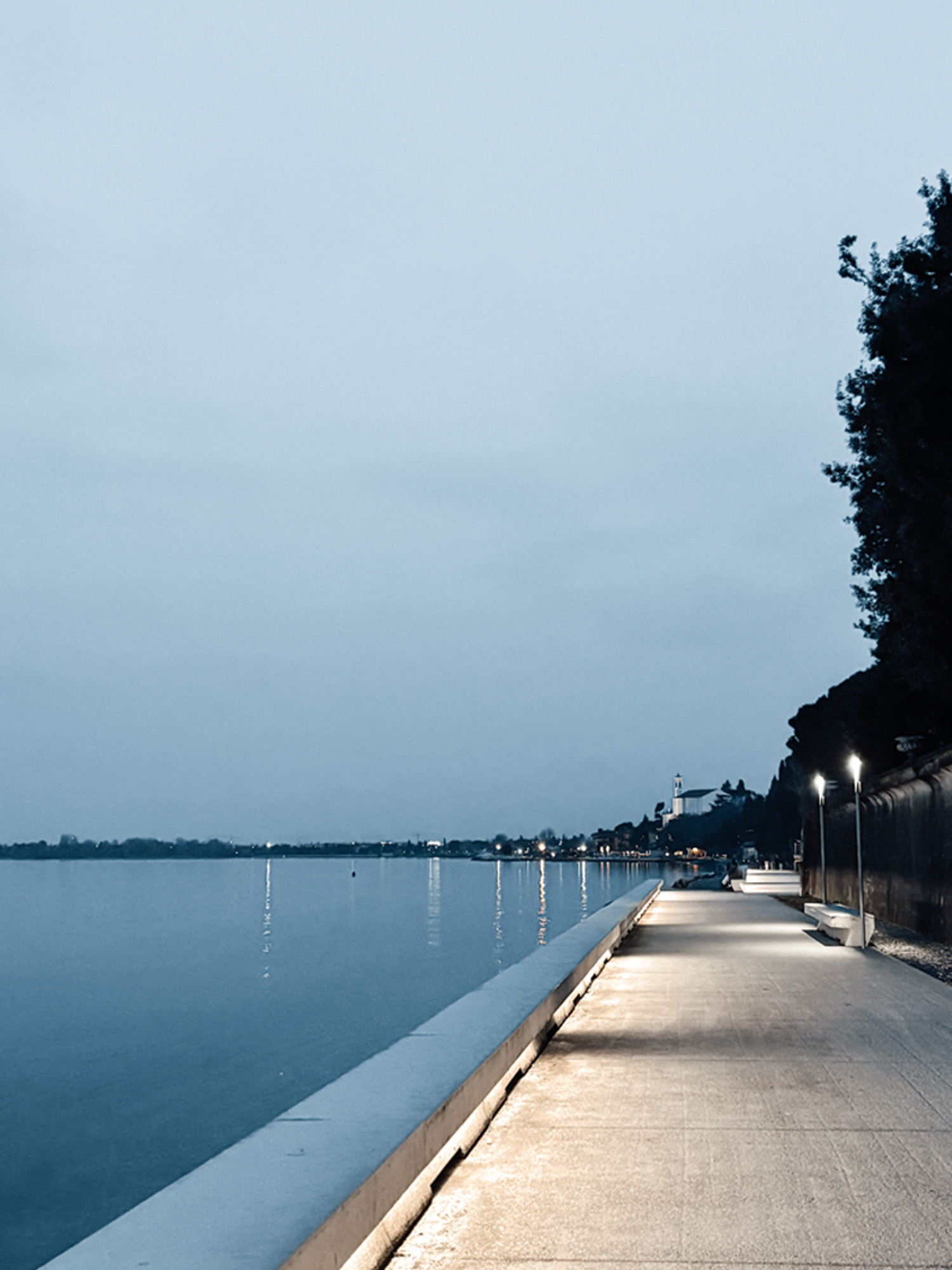 A lakeside promenade at dusk, path lights reflected in the water