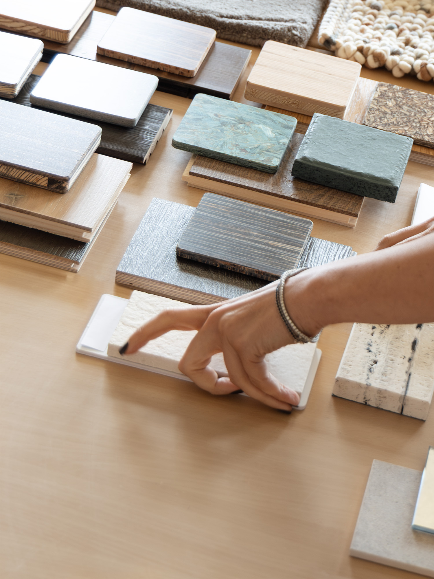 A hand selecting a material sample from a spread of wood, stone, and textile swatches