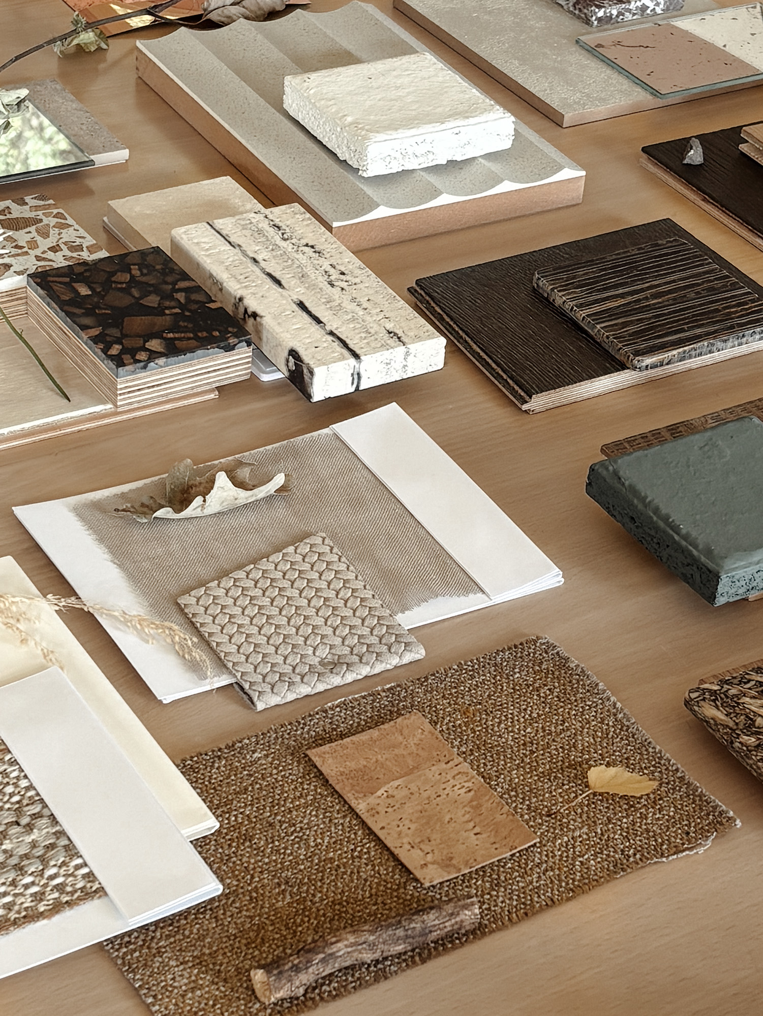 An overhead spread of material samples — stone, wood, textile, cork — paired with foraged natural elements