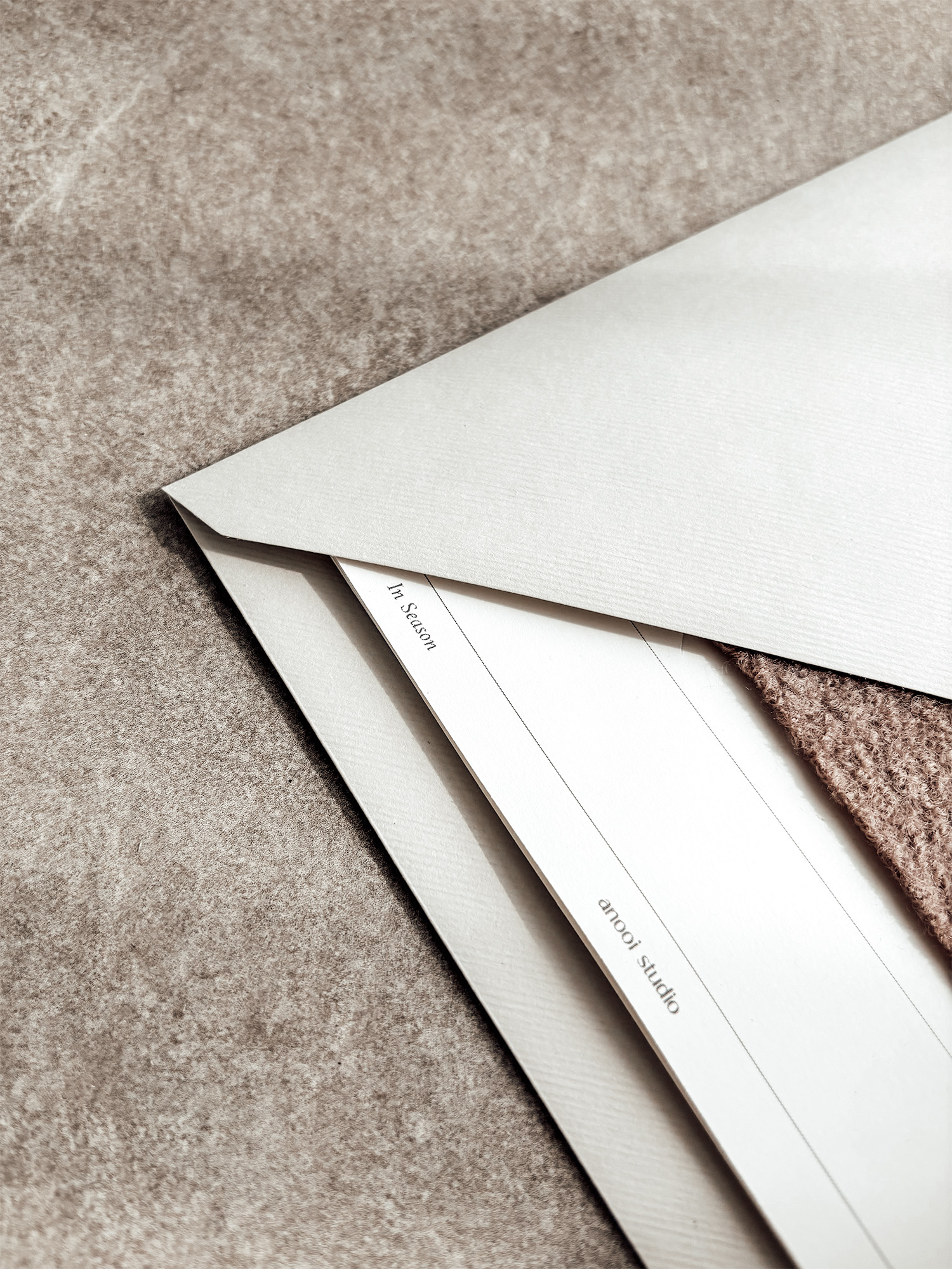 The corner of an envelope with In Season cards tucked inside, the edge of a wool sample visible