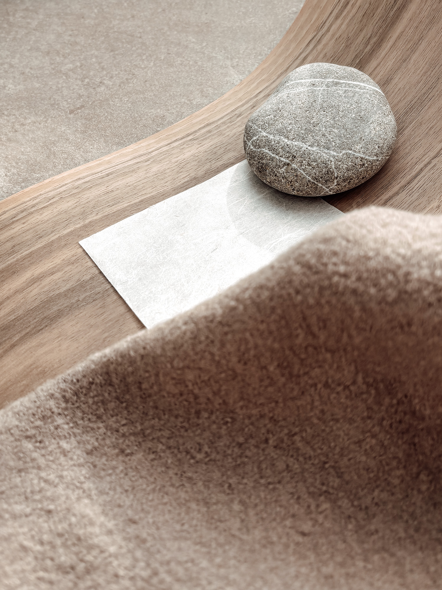 Material samples of wool, wood and paper beside a veined pebble, in soft daylight