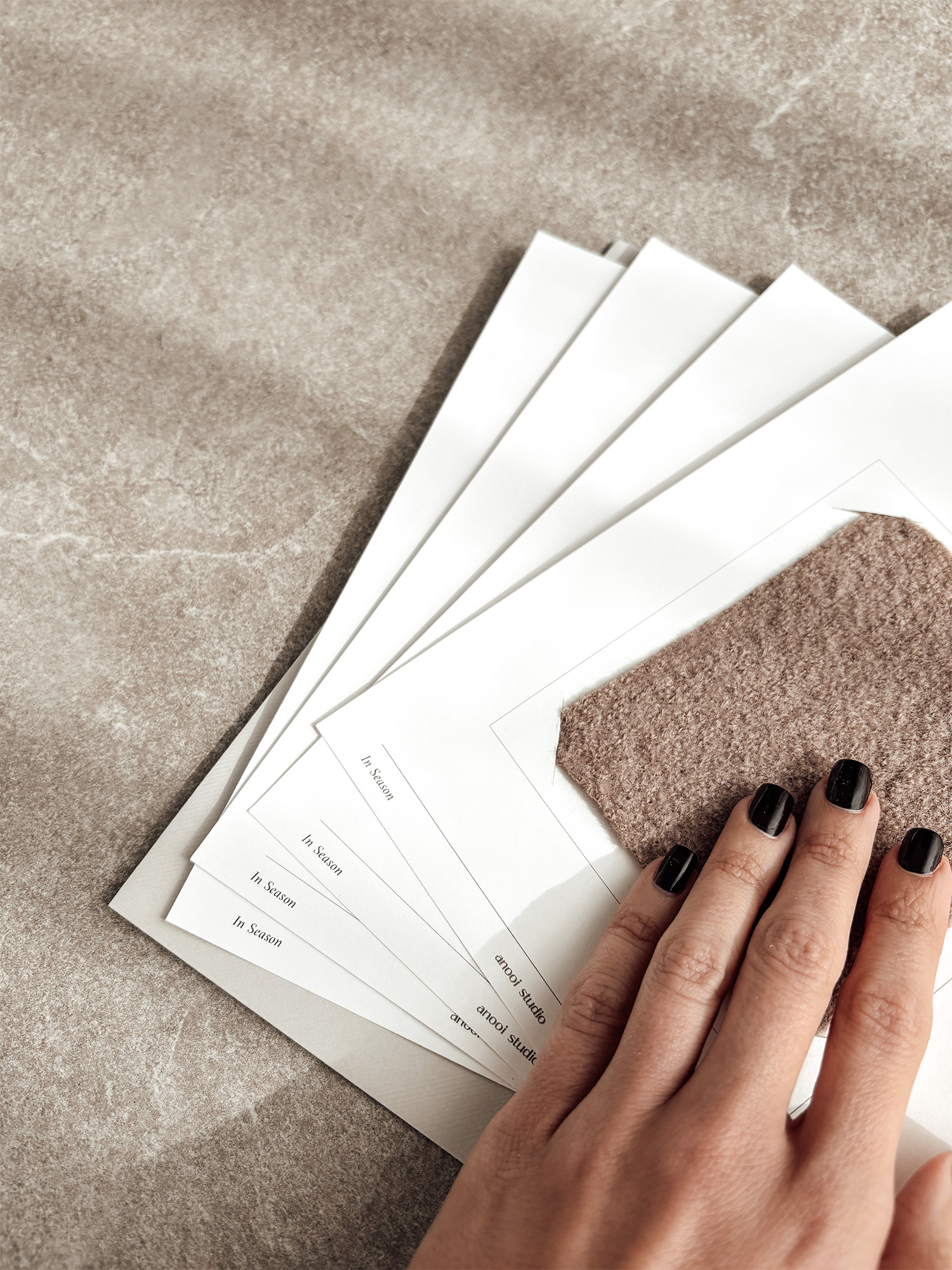 A hand resting on the wool sample of an In Season card, cards fanned on a stone surface