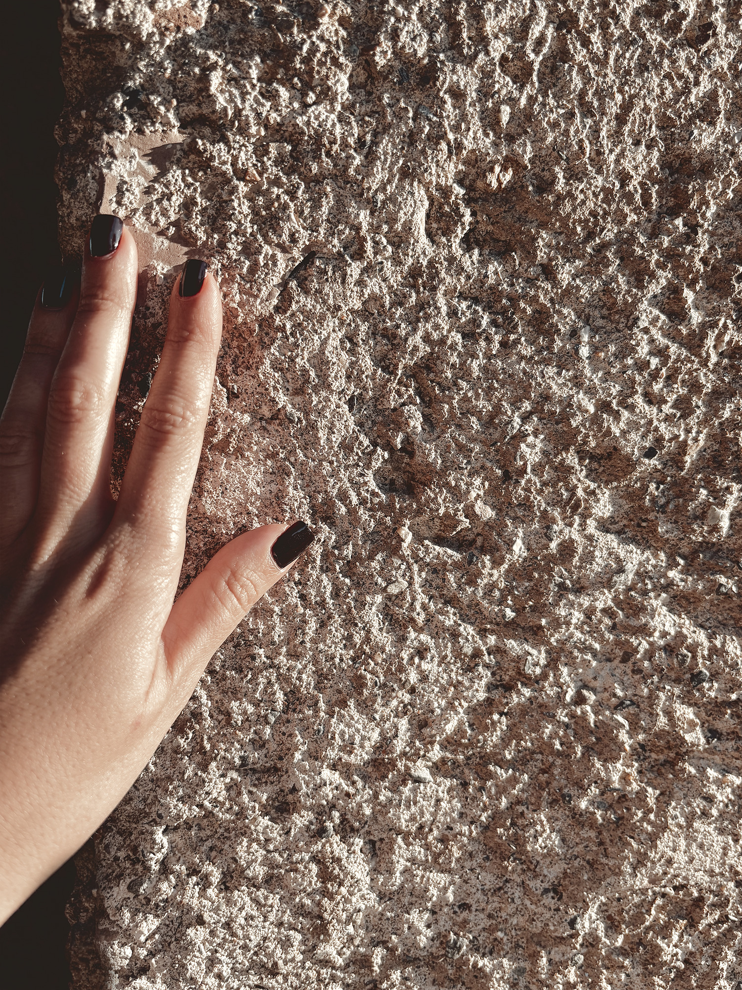 A hand resting against a rough, weathered wall in low sunlight, its coarse surface catching light and shadow